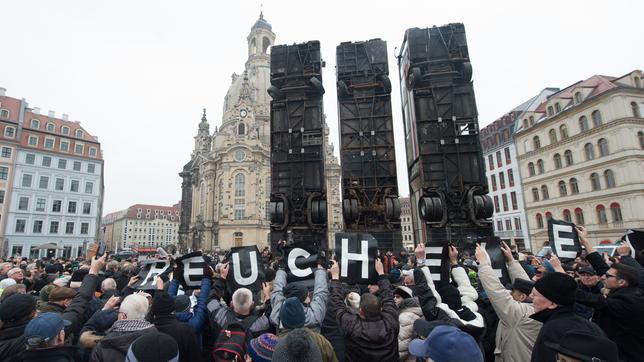 Menschen protestieren vor drei hochkant aufgestellten Bussen.