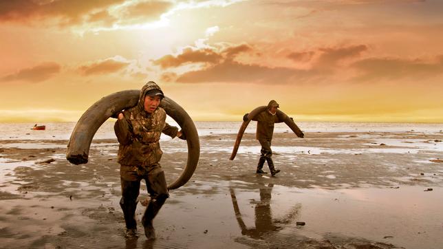 Bild: Rise and Shine Cinema Zwei Männer tragen Mammut-Stoßzähne über den Schultern.