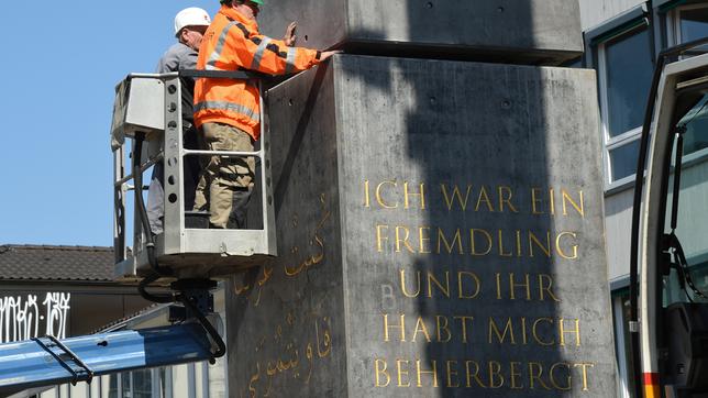 Zwei Bauarbeiter stellen einen Obelisk auf.