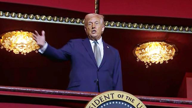 Ein älterer Herr mit grau-blondem Haar steht erhöht in einem feierlichen Raum mit Kronleuchtern. Er tägt einen blauen Anzug und gestikuliert. Es ist der US-Prsident Donald Trump.