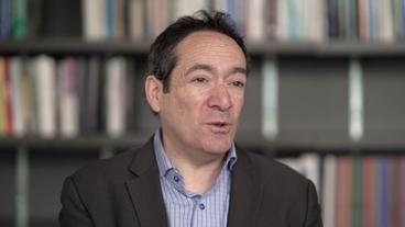Bild: NDR Ein mittelalter, Weißer Mann mit dunklen Haaren, blaues Hemd, graues Jackett, sitz vor einer Bücherwand. Es ist Jonathan Katz.