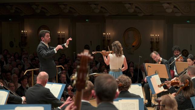 Ein Mann mit dunklen kurzen Haaren dirigiert ein Sinfonieorchester. Es ist der jüdisch-israelische Dirigent Lahav Shani.