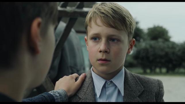 Ein blonder Junge schaut in die Kamera, eine Hand liegt auf seiner Schulter. Es ist ein Bild aus Fatih Akins Film "Amrum".