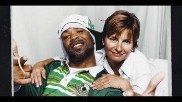 Bild: NDR Eine Person of Colour mit Basecap und in Hip-Hop-Pose wird von hinten von einer Weißen Frau mit kurzen braunen Haaren umarmt. Es sind Method Man und Eva Ries.