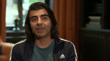 Bild: NDR Ein Mann mit halblangen schwarzen Haaren und grauer Trainingsjacke sitzt vor einem Fenster. Es ist der Regisseur Fatih Akin.