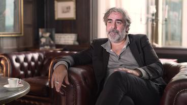 Bild: NDR Ein Mann mit halblangen grauen Haaren und Vollbart sitzt in einem braunen Ledersessel und raucht. Es ist Deniz Yücel vom PEN Berlin.