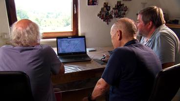 Drei Männer sitzen an einem Schreitisch vor einem Computer