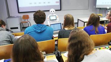 Studenten sitzen in einem Hörsaal und werden von einem Roboter unterrichtet.