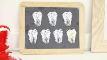 Sieben Zähne auf einer Kreidetafel, davon einer ein Kreidezahn