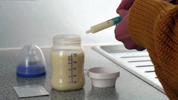 Mit einer Spritze wird ein Bakterienstamm in eine Babymilchflasche gegeben.