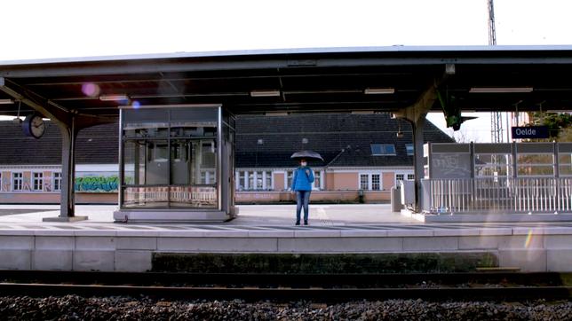 Frau wartet mit Sonnenschirm am Bahnsteig