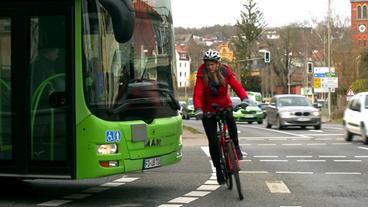 Ein Fahradfahrerin fährt an einem Bus vorbei.