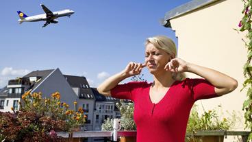 Eine Frau hält sich die Ohren zu, da hinter ihr ein Flugzeug startet.