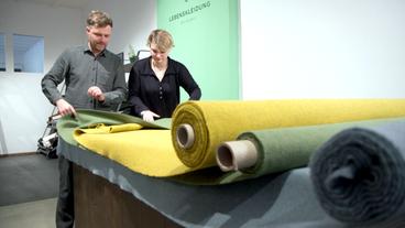 Bild: BR Betreiber der Textilagentur "Lebenskleidung" begutachten große Rollen mit gelben, grünen und grauen Woll-Fleece-Stoffen.