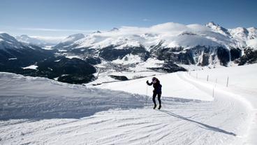 Bergpanorama, eine Frau läuft auf Skiern einen verschneiten Hang hinauf.