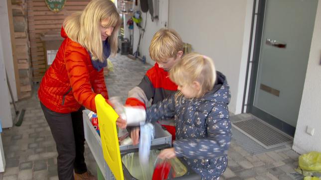 Mutter mit Kindern sortiert Plastikmüll in Gelben Sack