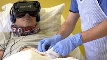 Ein Mann im Krankenhausbett wird medizinisch versorgt. Er trägt eine VR-Brille.
