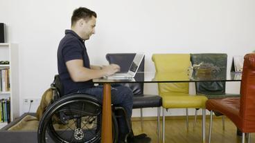 Thomas Binder im Rollstuhl bei der Arbeit am Laptop.