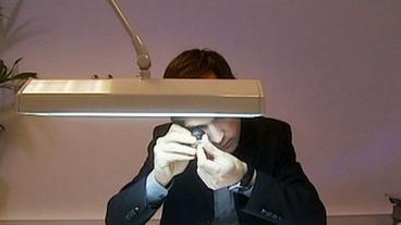 Mann am Schreibtisch kontrolliert unter einer Lampe einen Rohdiamant