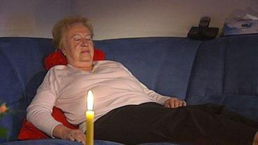 Frau schläft auf Sofa ein, am Tisch eine brennende Kerze