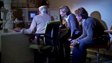 Zwei Forscher und Lennart Nilsson sitzen vor einem Monitor, die Forscherin guckt überrascht