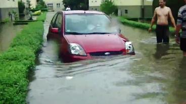 Menschen stehen bis zu den Knien im Wasser, ein Auto ist halb versunken