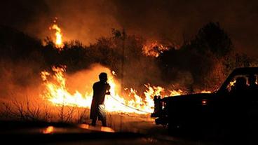 Brennende Savanne bei Nacht, im Vordergrund ein Mann, der versucht das Feuer zu löschen