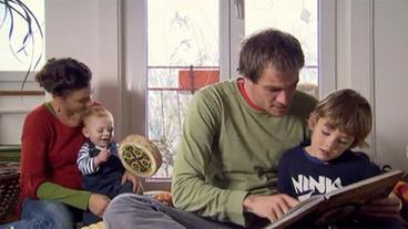 Vater Michael vorlesend mit größerem Sohn und von seiner Familie umgeben