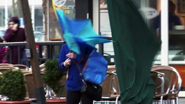 Ein Frau mit Regenschirm kämpft gegen den Wind an.