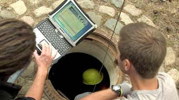 Wissenschaftler mit Laptop an einem Kanalschacht 