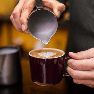 Barista gießt milchschaum zu Herzform in einer Kaffeetasse.
