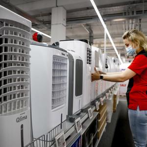 In einem Geschäft stehen Klimaanlagen, eine Verkäuferin richtet ein Gerät