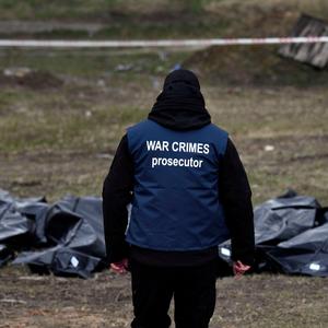 Kriegsverbrechen in der Ukraine - ein Mann steht vor Leichensäcken 