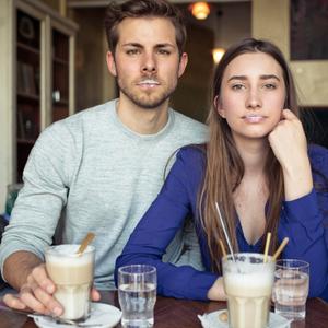 Mann und Frau mit Milchschaum an der Oberlippe und Kaffee mit Milch in Gläsern vor sich