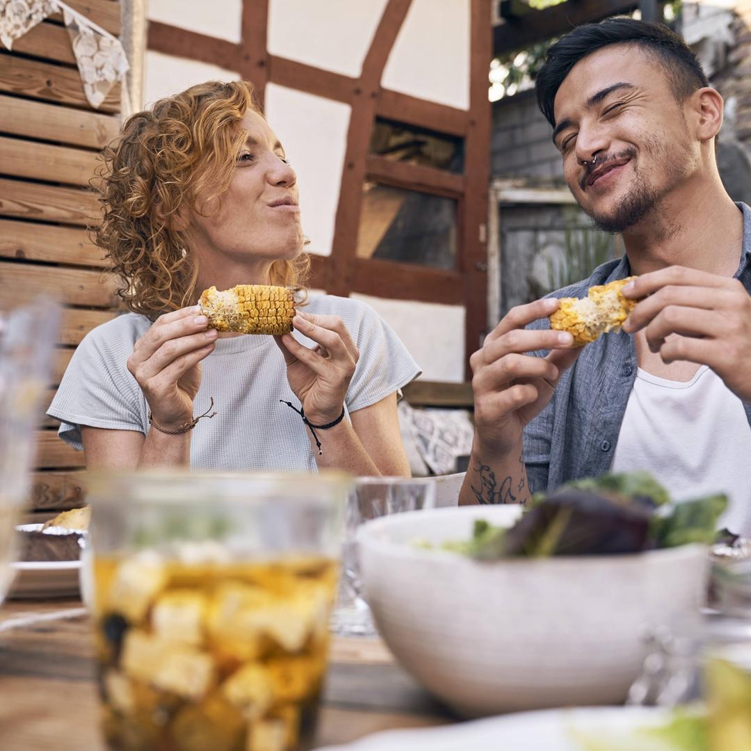 So schmeckt der Sommer: Drinks, Grillen und leichte Kost - eine Frau und ein Mann beißen in gegrillte Maiskolben