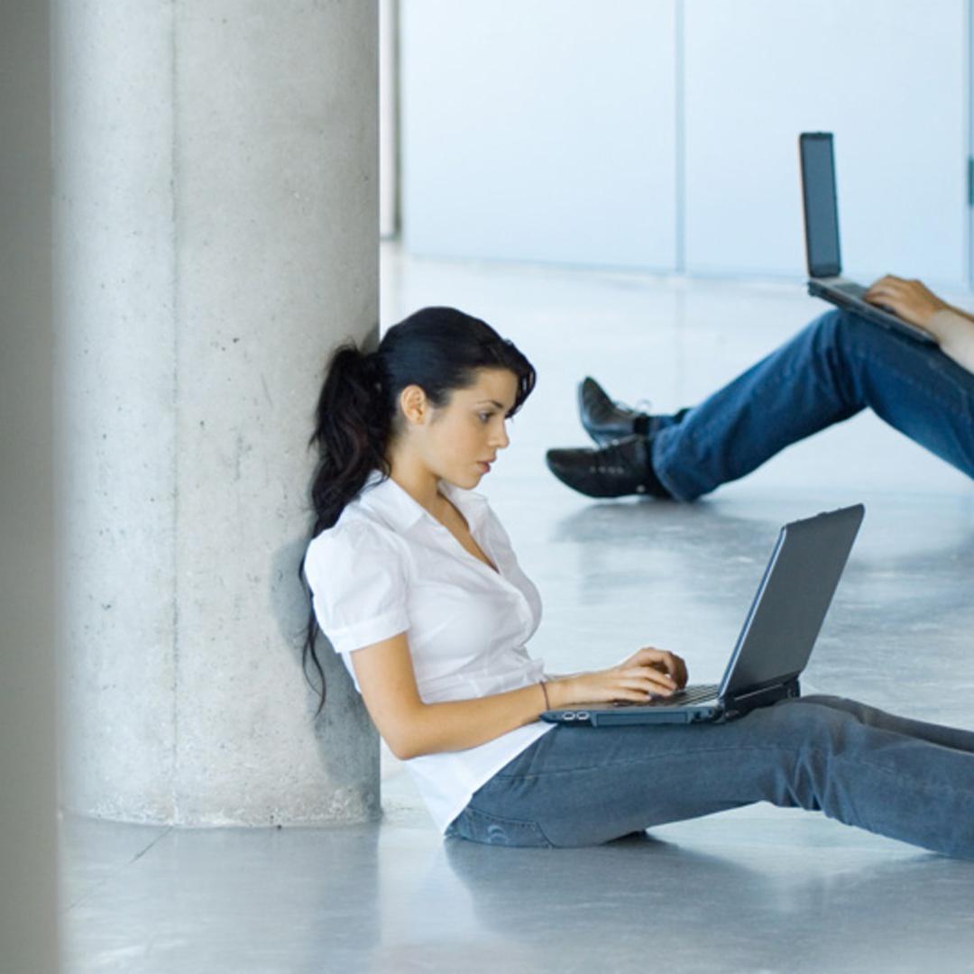 Zwei am Laptop arbeitende Menschen sitzen auf dem Boden. Zwei am Laptop arbeitende Menschen sitzen auf dem Boden.