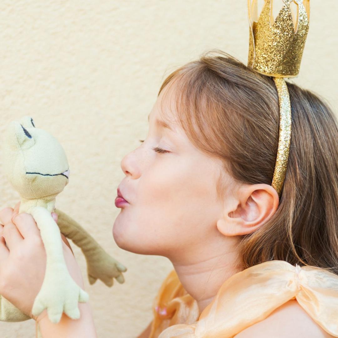 Als Prinzessin verkleidetes Mädchen küsst Frosch-Stofftier