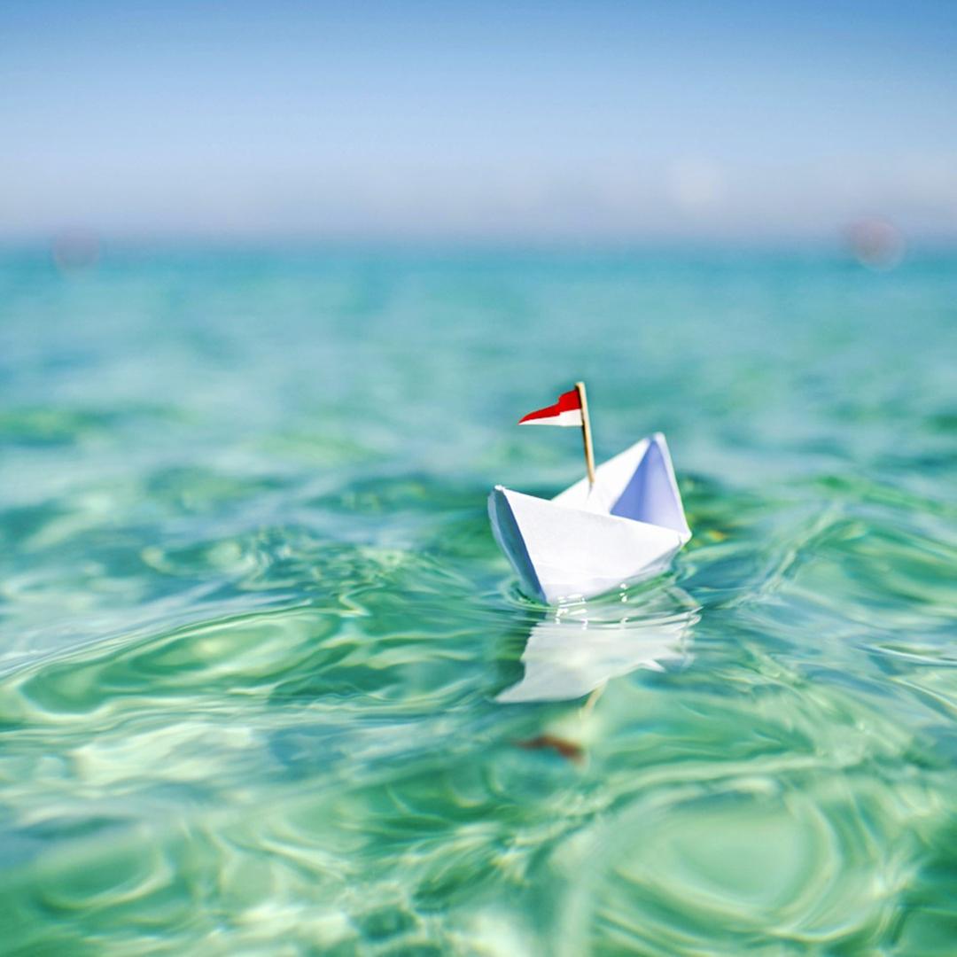 Papierschiffchen auf türkisblauem Wasser