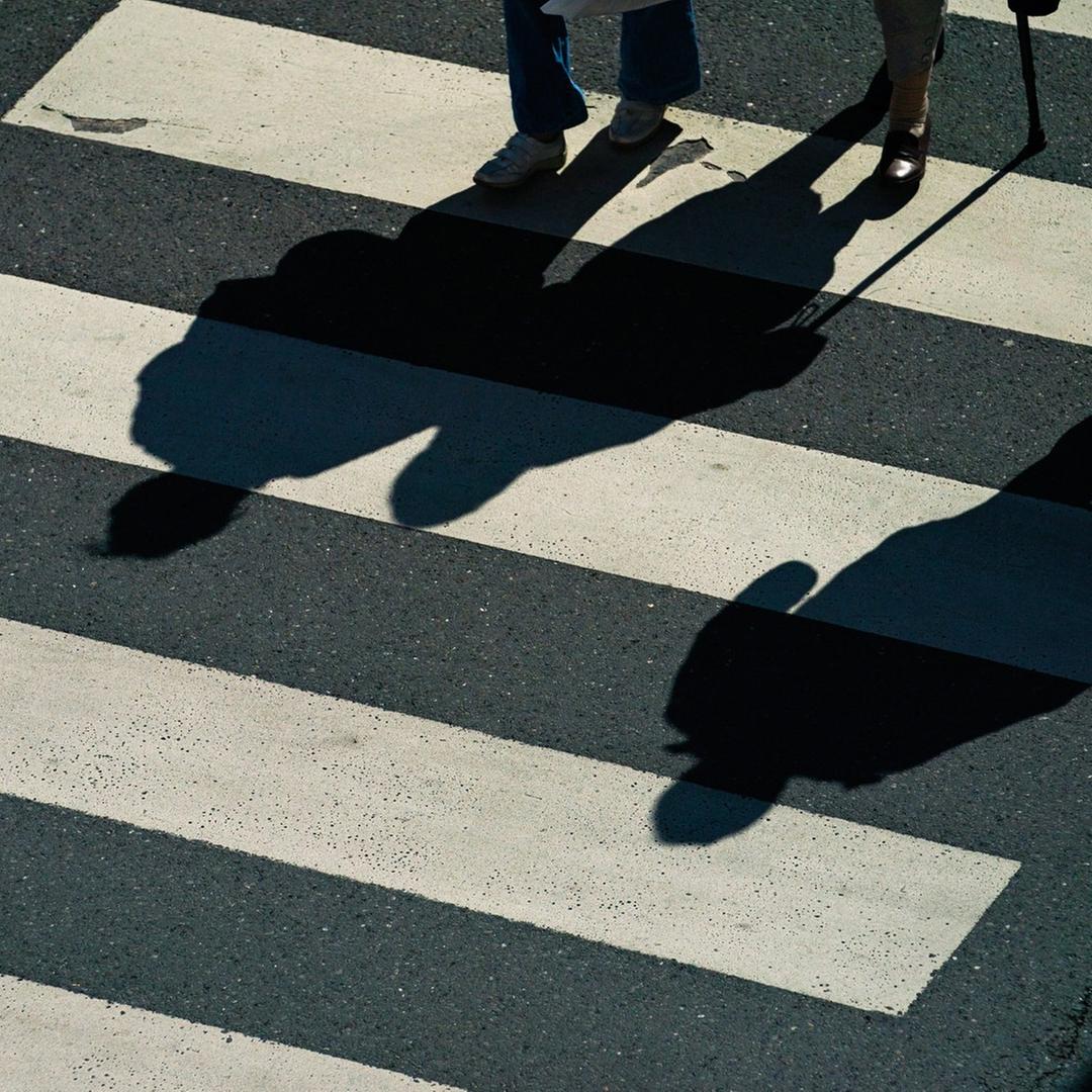 Passanten gehen über einen Zebrastreifen und werfen Schatten.