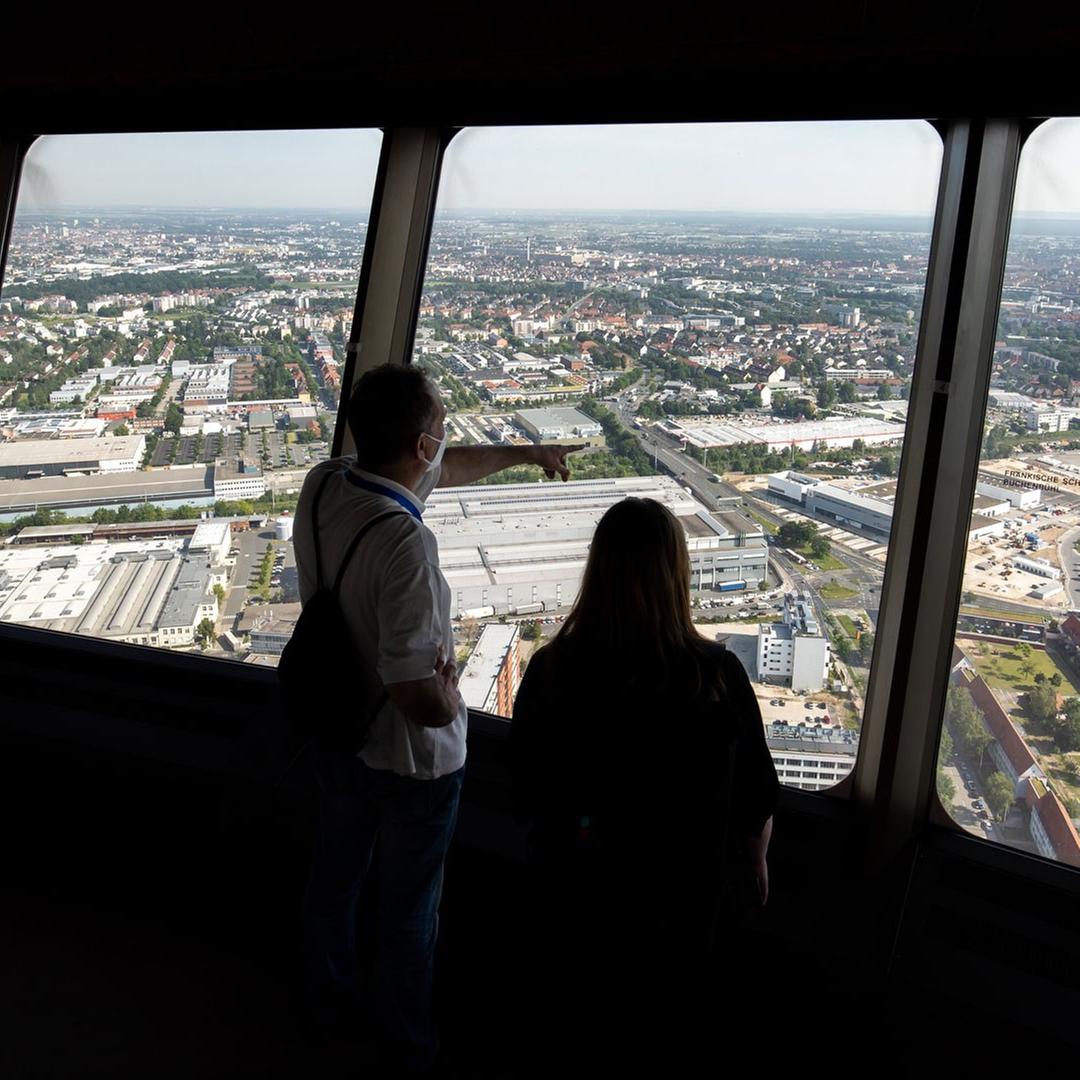 Zwei Menschen blicken aus einem Aussichtsturm über eine Stadt Zwei Menschen blicken aus einem Aussichtsturm über eine Stadt