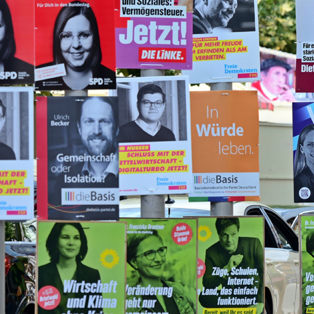 An Straßenlaternen hängen zahlreich Plakate von verschiedenen Parteien.