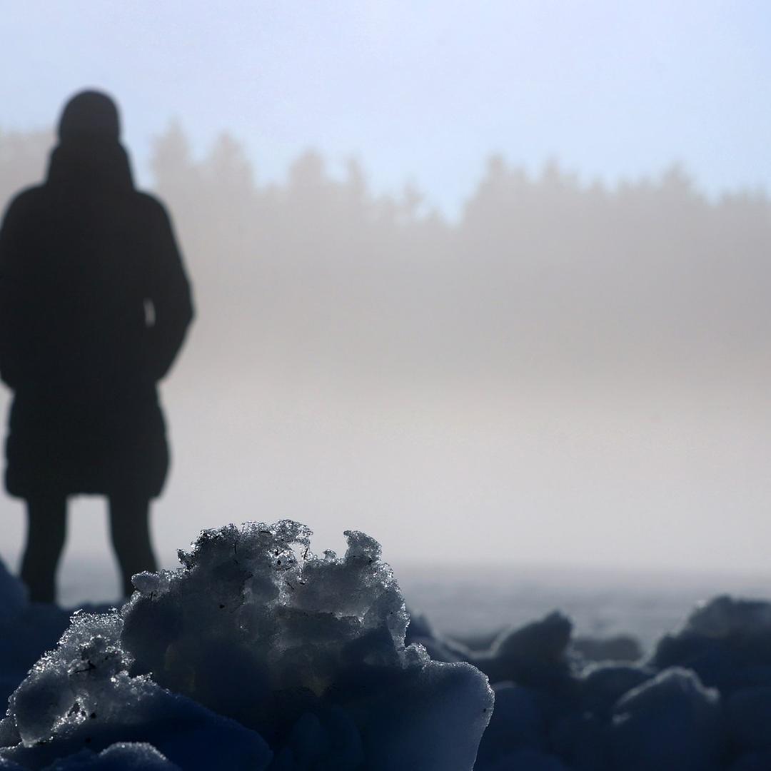 Eine Frau genießt vor im Sonnenlicht glitzernden Schnee den Sonnenschein. 