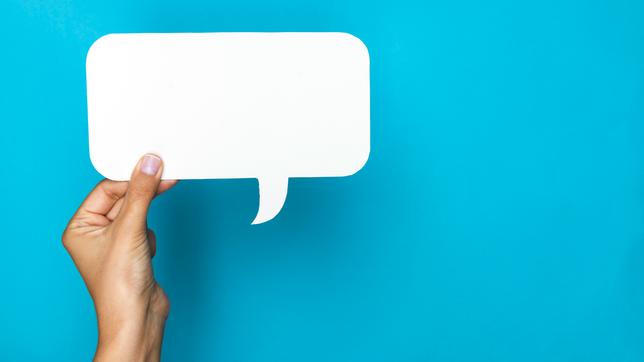Bild: iStock / Getty Images Plus/E+/simarik Hand hält eine weiße Sprechblase vor blauem Hintergrund.