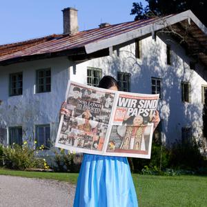 Schönste Erinnerungen verbindet Papst Benedikt mit Traunstein. Das Bild zeigt eine Frau in Tracht mit der Bild-Schlagzeile Wir sind Papst im Hintergrund das ehemalige Familienhaus der Ratzingers.