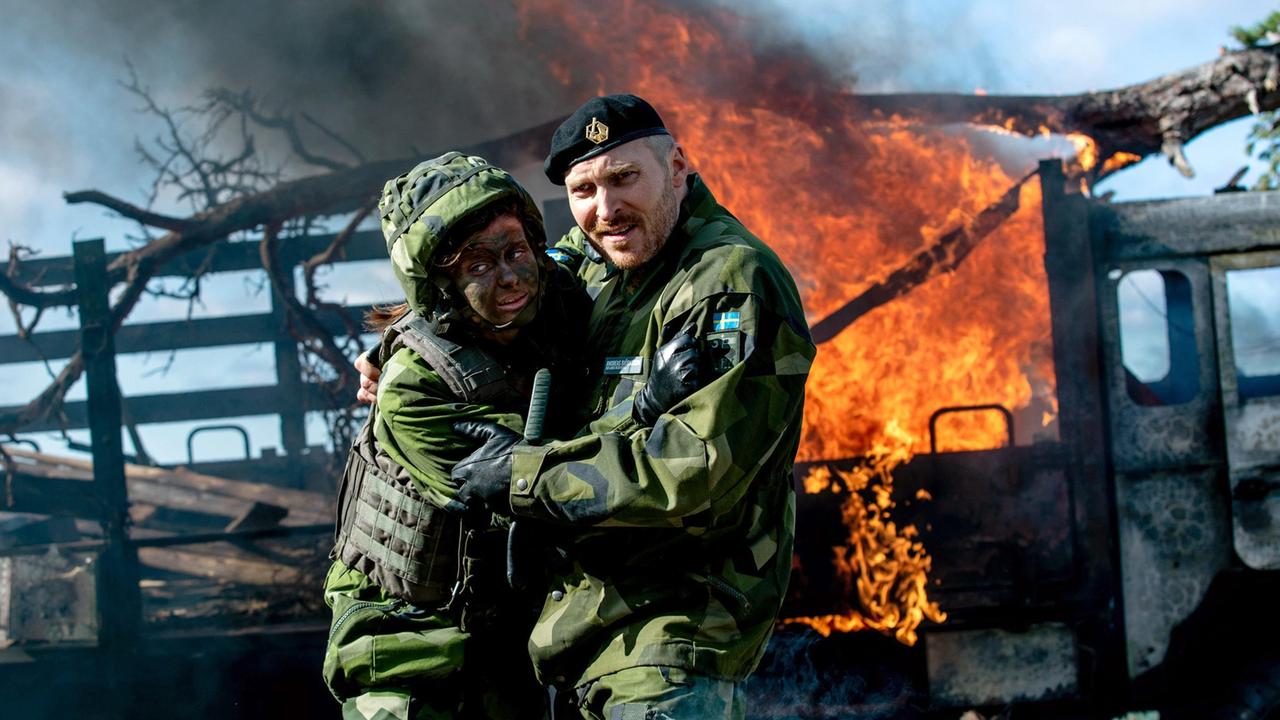 Andreas Björnsonn (Jakob Hultcrantz Hansson) zieht die Rekrutin Isabell (Hanna Ardéhn) vom explodierenden Truppenfahrzeug weg.