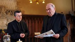 Bischof Momsen liest mit düstere Miene die Zeitung. Neben ihm steht Domkapitular Stölzer. 