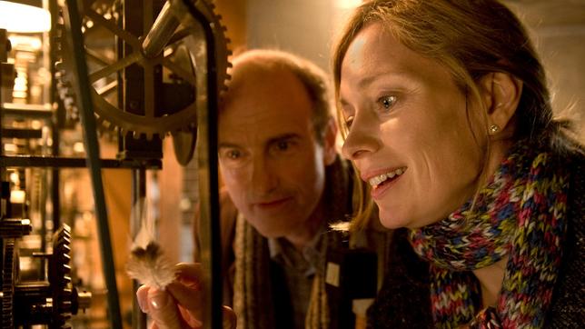 Karina (Katja Weitzenböck) zeigt Rudolf (Johannes Herrschmann) eine Vogelfeder, die das Uhrwerk der Kirchturmuhr blockiert.
