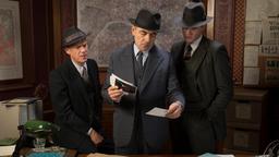 Mit seinen Teamkollegen Inspektor Janvier (Shaun Dingwall, li.) und Inspektor LaPointe (Leo Staar, re.) geht Maigret (Rowan Atkinson) Tatortfotos durch, in der Hoffnung auf eine Spur.