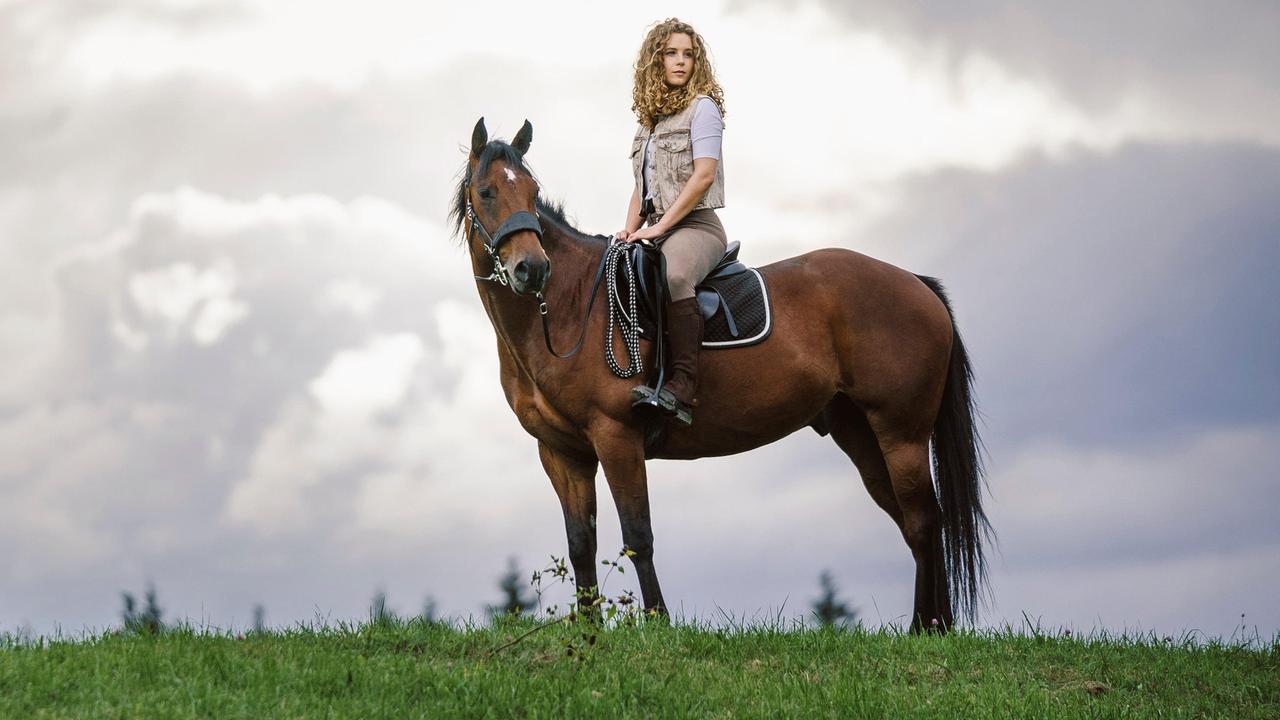 Rike (Klara Deutschmann) trabt mit Jacomo am Waldrand entlang.