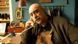 Schuh Ali (Özgür Karadeniz) sitzt in seinem Geschäft und telefoniert.